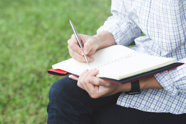 istock close up hand people man are sitting on a chair wooden. using pen writing Record Lecture note pad into the book in park public. top view 1146901839