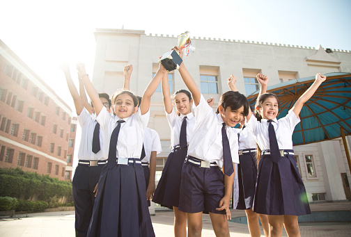 Cheerful school students holding trophy and celebrating victory