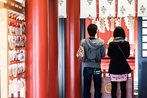 Tokyo, Japan - March 31, 2018: Shinto temple near Hie shrine entrance withback of young couple praying at altar inside