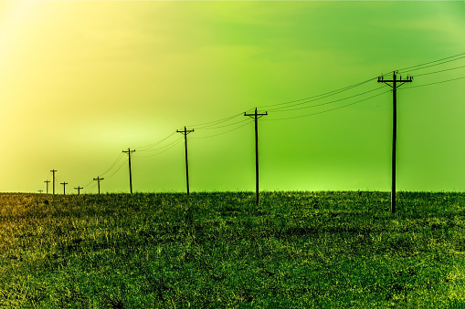 Electric poles in a rural area with green yellow sky, green energy