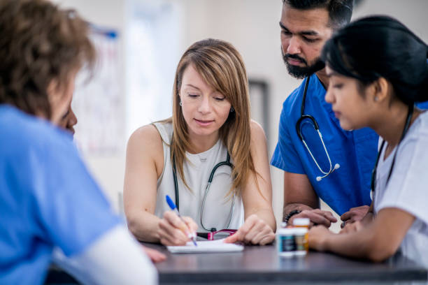 Doctor's meeting A multi-ethnic group of doctors are indoors in an office. They are gathered around a table for a meeting. One woman is taking notes. team event stock pictures, royalty-free photos & images