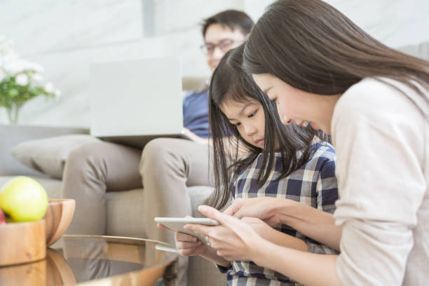 happy asian family spending time together on sofa in living room. family and home concept - father digital tablet asian ethnicity daughter imagens e fotografias de stock