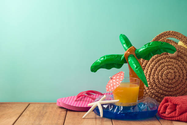 istock Summer vacation background with orange juice, beach items and pool float on wooden table 1146920345