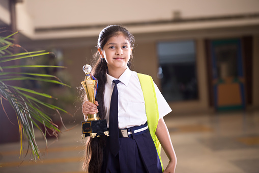 Pequeña chica sosteniendo trofeo en el campus escolar photo
