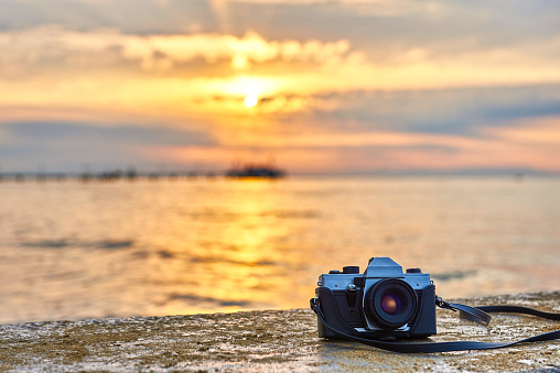 Vintage film photo camera. Front view, close up photo. Against the background of the sea. Beautiful sunset, waves and landscape.