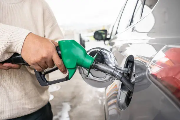 Photo of Hand refilling the car with fuel at the refuel station. Grey car at gas station being filled with fuel at New Zealand. Handle fuel nozzle to refuel. Vehicle fueling facility.