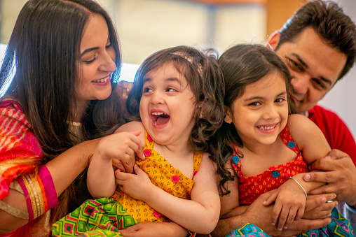 An Indian family featuring two young parents and their young  daughters are spending time with one another and laughing together inside their home