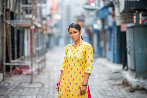 An Indian woman stands in the middle of the street outside. She is beautifully dressed.