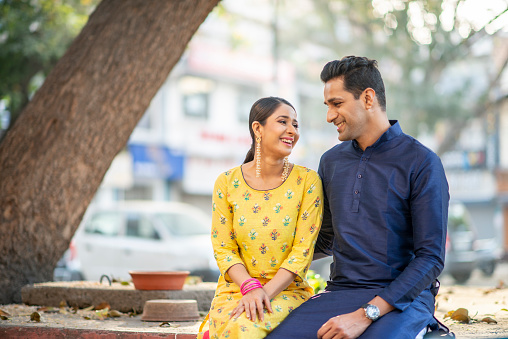 An Indian couple sits side by side while looking at each other lovingly. They are incredibly happy.