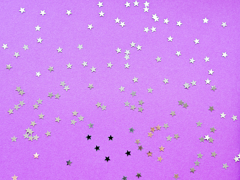 Holiday background with silver star confetti on violet background. Flat lay, top view.