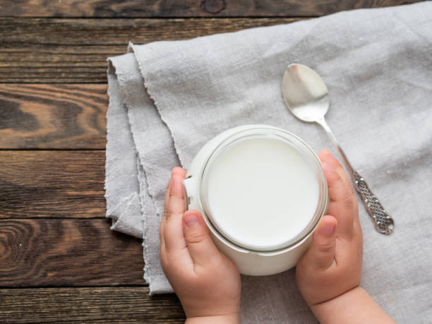 naturalny domowy jogurt w szklanym słoiku. zdrowe jedzenie na śniadanie w rękach dziecka. dziecko trzymające słoik z kwaśną śmietaną na lniany obrus na drewnianym stole. - yogurt jar cream milk zdjęcia i obrazy z banku zdjęć