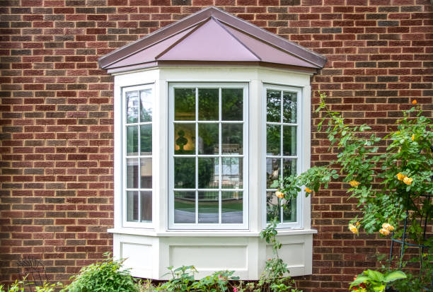 Bay window with copper roof on traditional brick home with flowers below and yellow roses extending out onto the window in springtime Bay window with copper roof on traditional brick home with flowers below and yellow roses extending out onto the window in springtime bay window stock pictures, royalty-free photos & images