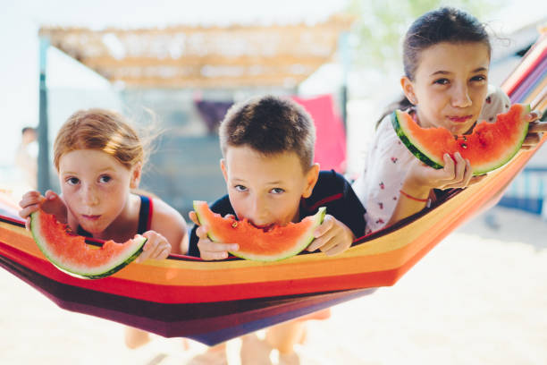 Cute kids lying down on hammock and eating watermelon