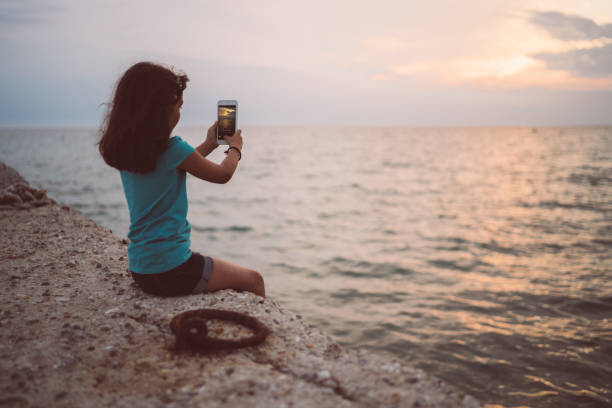 Girl sitting at the quay and taking photo with smartphone