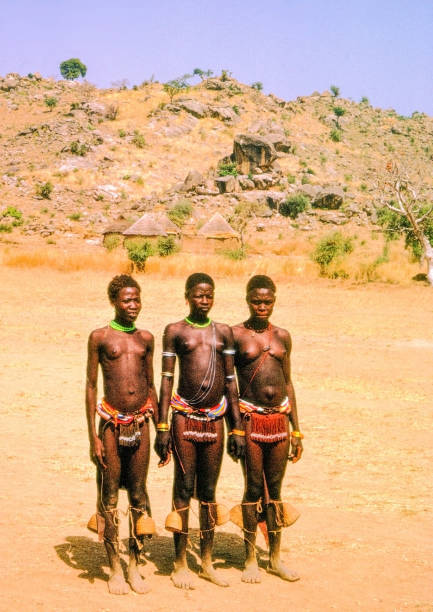 Nostalgia. Cameroon 1965. Tree young women redy to dance. It is midday with shadows  showing the sun at zenit. Very dry climate. Traditional huts in the background.\n\n+++ scanned slides from 1965 +++