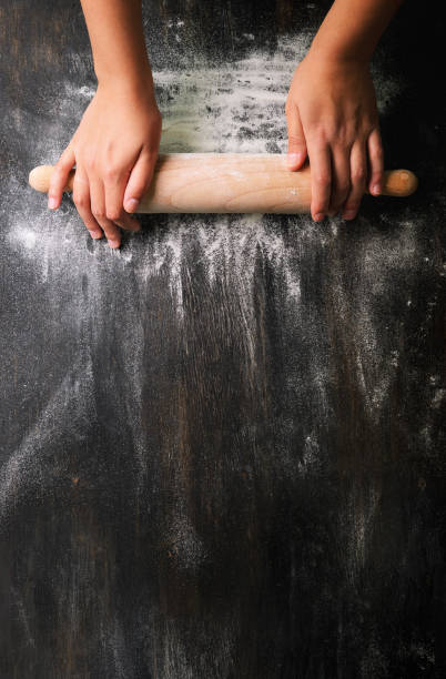 Girl hands keep rolling pin with flour on dark black table, baking background, top view, copy space for your text, meru, recipe. Banner