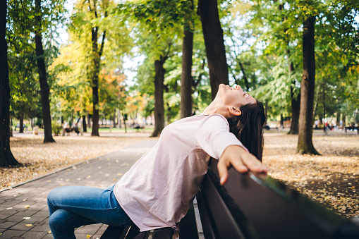 Young woman sitting on a bench in a public park, relaxing, enjoying.