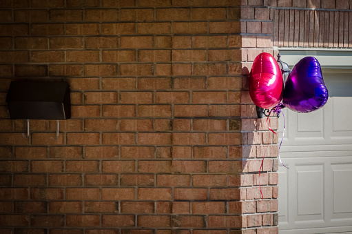 Collored Party balloons and mailbox  on the exterior of a brick house in the bright sunlight