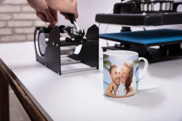 Man printing on coffee mugs in workshop
