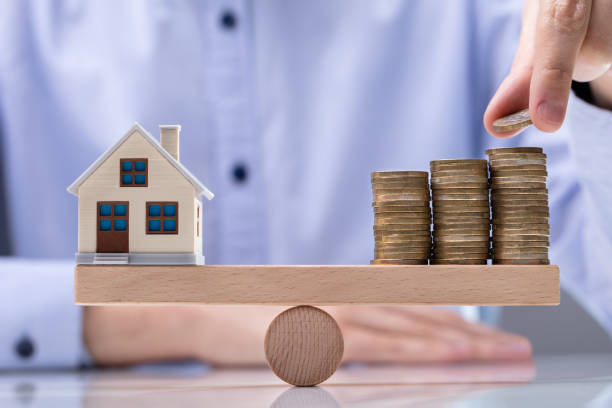 istock Model House And Stack Of Coins On Seesaw 1146965426
