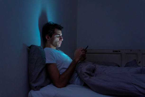 retrato de estilo de vida del hombre adicto al teléfono celular despierto tarde en la noche en la cama usando el teléfono inteligente comprobando gustos y seguidores, chateando, coqueteando, saliendo en las redes sociales. adicción a internet y abuso m� - working bed smart phone bedroom fotografías e imágenes de stock