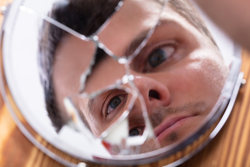 Close-up Of Young Man Looking At His Face In A Broken Mirror