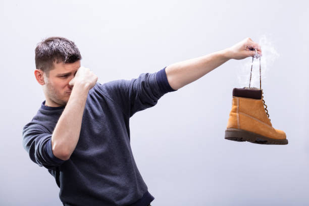 istock Man Covering His Nose While Holding Stinky Shoe 1146967203