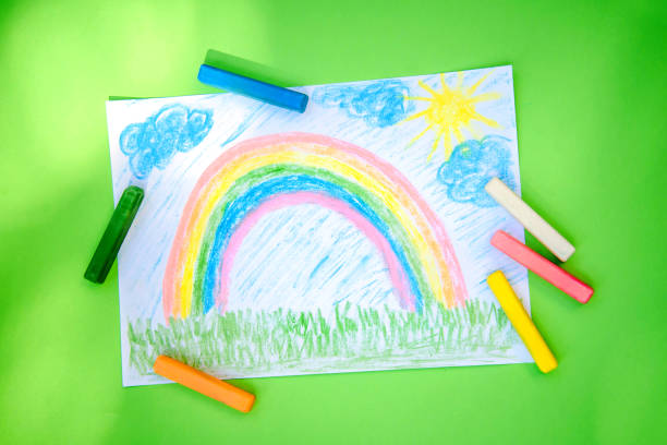 Children drawing rainbow colored crayons on a bright green background on a sunny day
