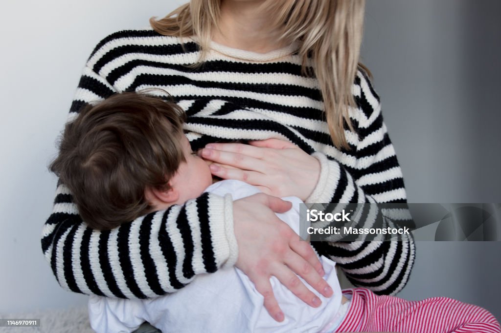 Young mother breastfeeding toddler boy in striped sweater Feeding Stock Photo