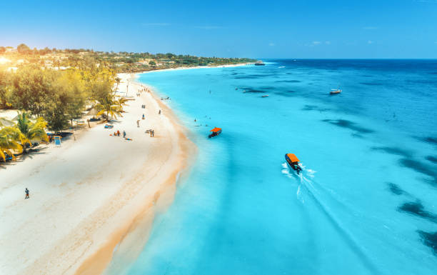 vista aerea delle barche sulla costa tropicale con spiaggia sabbiosa al tramonto. vacanze estive sull'oceano indiano, a zanzibar, africa. paesaggio con barca, palme, acqua blu trasparente, alberghi. vista dall'alto - nobody africa summer tourist resort foto e immagini stock