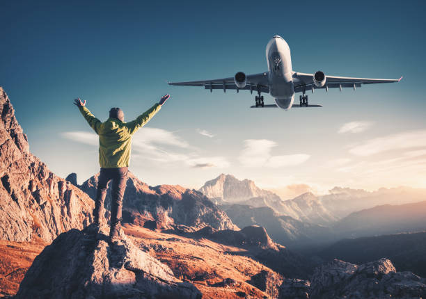 avión y hombre en la piedra con las armas levantados contra las montañas al atardecer. hombre deportivo feliz, avión de pasajeros volando, rocas y cielo azul en los dolomitas, italia. los aviones de viajero y aterrizaje - leaving business landscape men fotografías e imágenes de stock