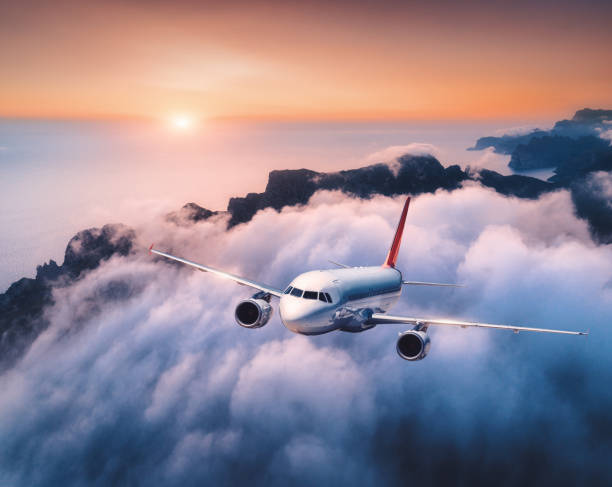 istock Passenger airplane is flying over clouds at sunset. Landscape with white airplane, low clouds, sea coast, orange sky at dusk. Aircraft is take off. Business trip. Commercial plane. Travel. Aerial view 1146972188