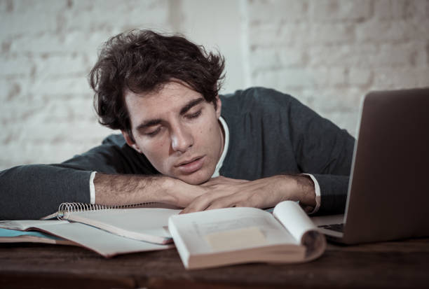 Overworked and tired male student working late at night on laptop trying not to fall asleep feeling fatigued, worried and sad. Moody dark light. Finals exams Online learning and overwork concept. estudiante con exceso de trabajo y cansado trabajando hasta tarde en la noche en el ordenador portátil tratando de no conciliar el sueño sintiéndose fatigado, preocupado y triste. luz oscura de mal humor. exámenes finales de aprendizaje en línea y con