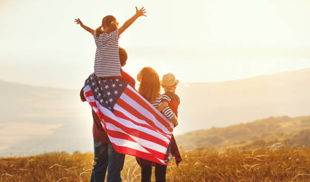 glückliche familie mit fahne von america usa bei sonnenuntergang im freien - patriotismus stock-fotos und bilder