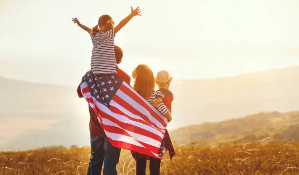 Photo of happy family with flag of america USA at sunset outdoors