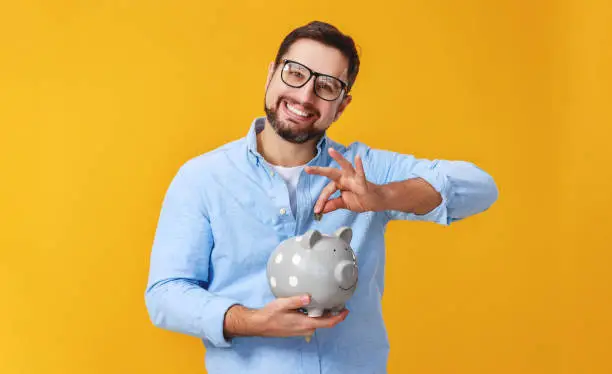 Photo of concept of Finance and business.  man with  piggy Bank on  yellow background color