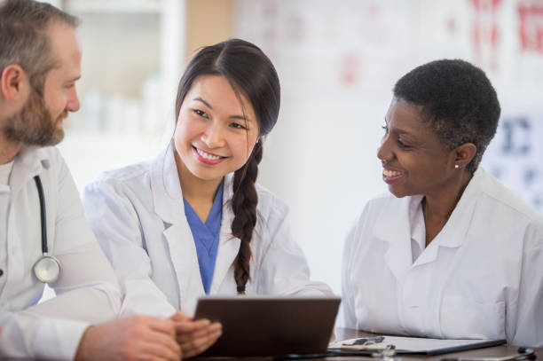 Doctors having a discussion Three medical professionals are sitting in an office having a meeting. One of them is holding an electronic tablet as she speaks to her coworkers. civilian stock pictures, royalty-free photos & images
