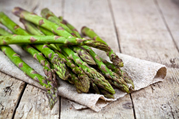 Bunch of fresh raw garden asparagus closeup and linen napkin on rustic wooden table background. stock photo