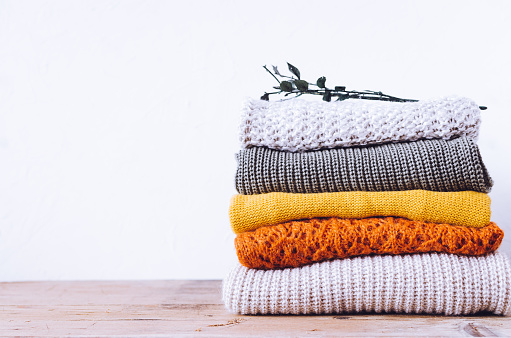 Pile of knitted woolen sweaters autumn colors on wooden table. Clothes with different knitting patterns folded in stack. Warm cozy winter fall knitwear concept. Copy space.