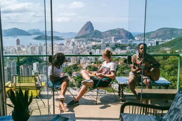Elevated view of Rio de Janeiro cityscape, man playing guitar with two friends relaxing and listening in sunlight