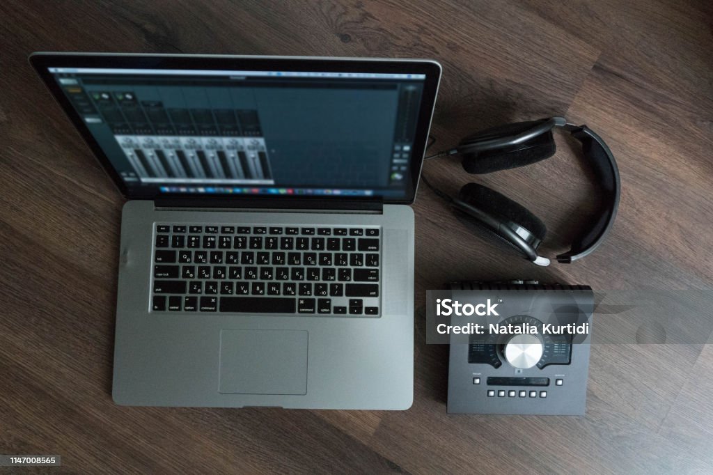 Flat lay of sound designers tools on dark wood table: laptop with mixing scene, sound card, headphones, microphone. Sound engineering tools. Professional sound card for music mixing and mastering Audio Equipment Stock Photo