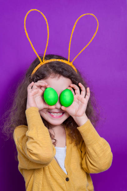 istock Girl with bunny ears with two Easter eggs on a colored background. 1147033958
