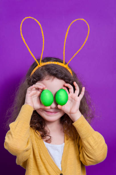 istock Girl with bunny ears with two Easter eggs on a colored background. 1147034082