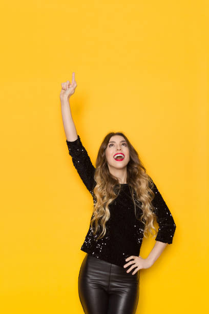 istock Young Woman In Black Sequin Sweater Is Pointing Up And Talking 1147040716
