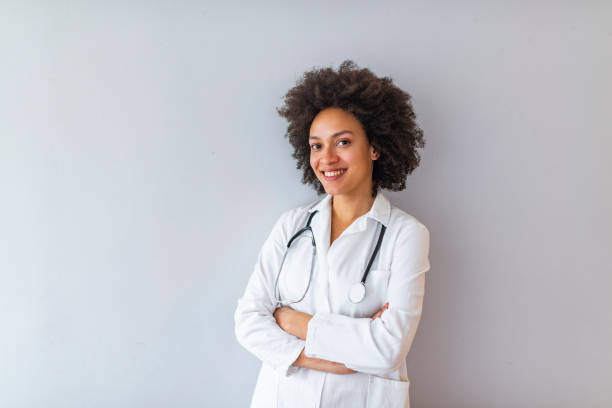 Woman hospital worker looking at camera and smiling Medical concept of young beautiful female doctor in white coat with phonendoscope, waist up. Woman hospital worker looking at camera and smiling, studio, grey background photography healthcare and medicine studio shot vertical stock pictures, royalty-free photos & images