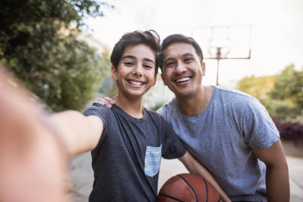 padre y hijo hispanos tomando una autofoto al aire libre mientras jugaba al baloncesto - bouncing ball family playing fotografías e imágenes de stock