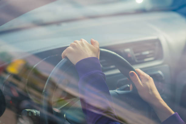 istock Young woman's hand holding on black steering wheel while driving in the car. view from the outside of the car 1147072292