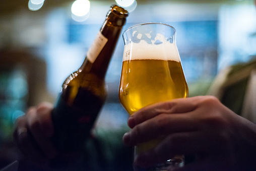 man's hand holds a bottle and glass of beer in bar