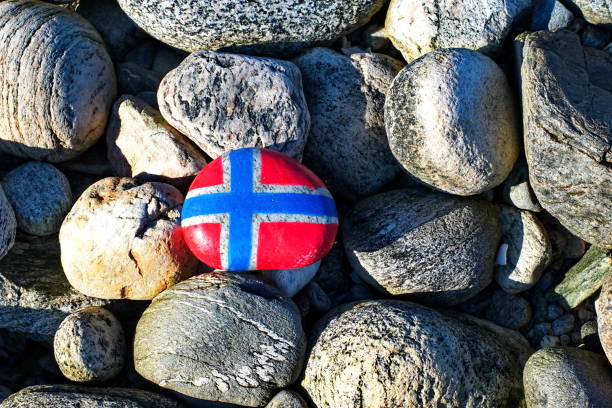 Image of the flag of Norway on a stone, between sea pebbles and seashells. Concept of Norwegian Constitution Day.  Celebrated on May 17.