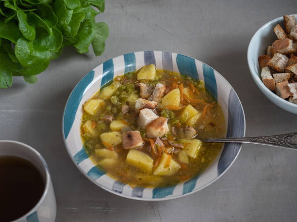 istock Pea soup in a deep striped ceramic plate with crackers on a white table. A mug of tea and leaf salad. 1147079576